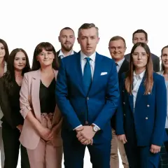 Grupa profesjonalistów w garniturach i kostiumach, stojąca przed białym tłem.