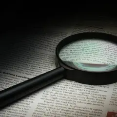 Lupa powiększa tekst, symbolizując dociekliwość i spostrzegawczość – kluczowe cechy dobrego detektywa.