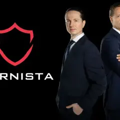 Dwaj mężczyźni w garniturach stoją obok logo "KARNISTA" na czarnym tle.