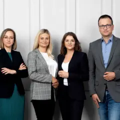 Cztery osoby w strojach biznesowych stoją przed jasną ścianą.
