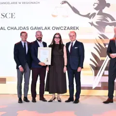 Pięć osób w garniturach i sukience stoi na scenie, odbierając nagrodę.