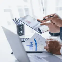 Dwóch mężczyzn w garniturach analizuje wykresy na tablecie i papierze.