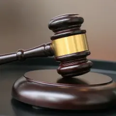 Drewniany młotek sędziowski ze złotym pierścieniem na ciemnej powierzchni.