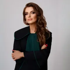 Kobieta w todze adwokackiej, z rękami skrzyżowanymi na piersi, na jasnym tle.