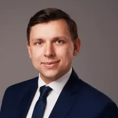 Portret mężczyzny w granatowym garniturze i krawacie na szarym tle.