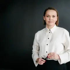 Kobieta w białej koszuli i czarnych spodniach na ciemnym tle.