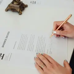 Dłoń podpisuje dokument "DIVORCE DECREE". Dowiedz się, jak napisać pozew o rozwód bez orzekania o winie.