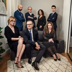 Grupa prawników w eleganckich strojach pozuje do zdjęcia w nowoczesnym wnętrzu.