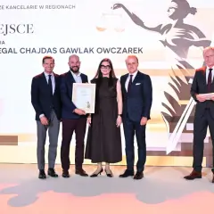 Pięć osób w eleganckich strojach pozuje do zdjęcia na tle sceny z grafiką i napisem "I MIEJSCE".