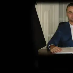 Mężczyzna w garniturze siedzi przy biurku z dokumentami.