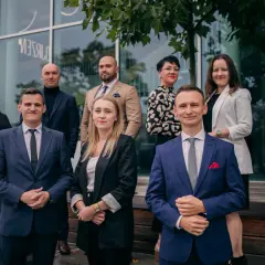 Grupa prawników w eleganckich strojach pozuje przed nowoczesnym budynkiem.