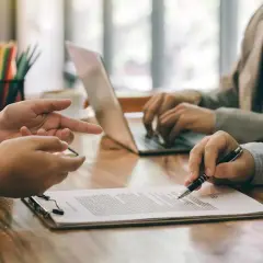 Ludzie w garniturach przy biurku omawiają dokumenty i korzystają z laptopa.