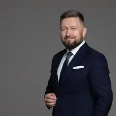 Portret mężczyzny w granatowym garniturze, białej koszuli i zielonym krawacie, z brodą i niebieskimi oczami.