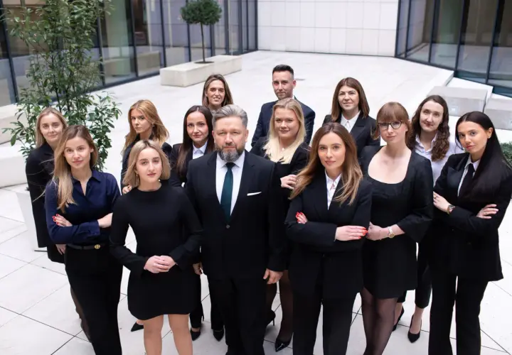 Grupa prawników w garniturach i sukienkach stoi przed nowoczesnym budynkiem.