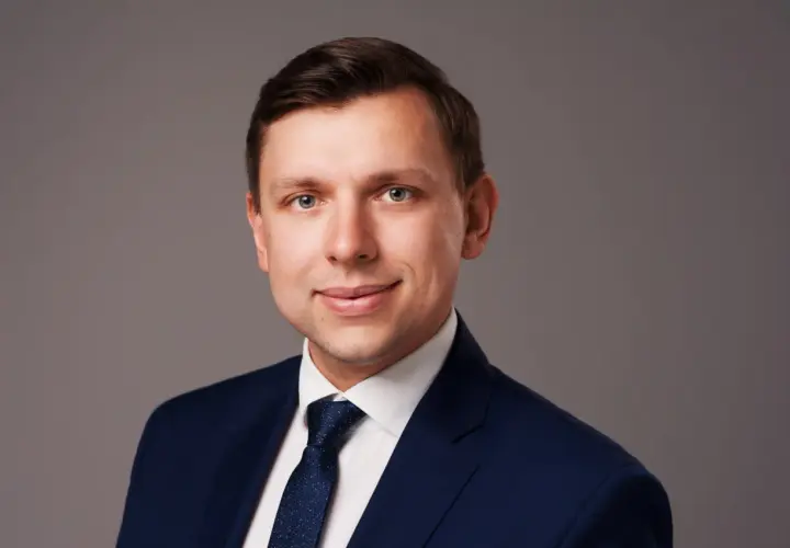 Portret mężczyzny w granatowym garniturze i białej koszuli z krawatem.