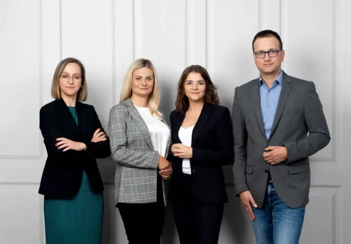 Cztery osoby w strojach biznesowych stoją przed jasną ścianą.