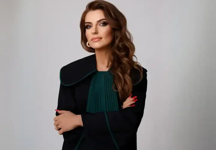 Kobieta w todze adwokackiej, z rękami skrzyżowanymi na piersi, na jasnym tle.