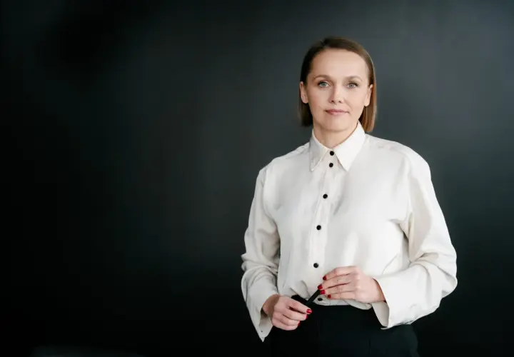 Kobieta w białej koszuli i czarnych spodniach na ciemnym tle.