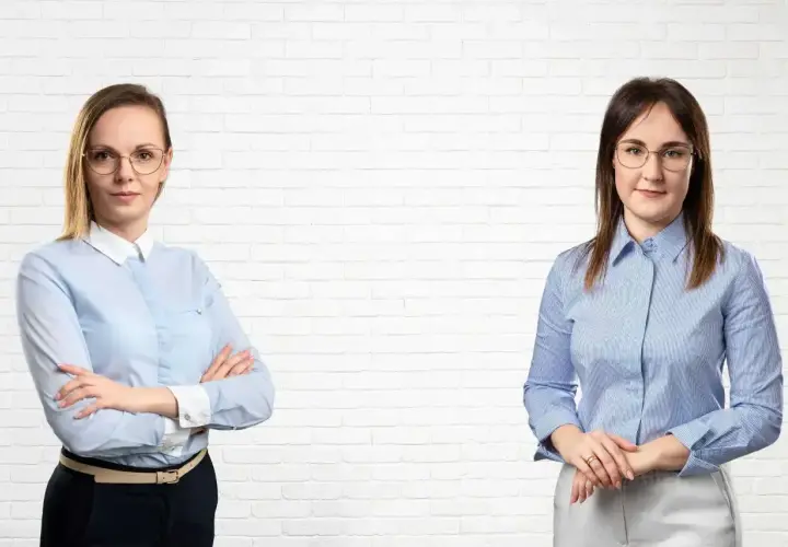 Dwie kobiety w koszulach na tle białej cegły.