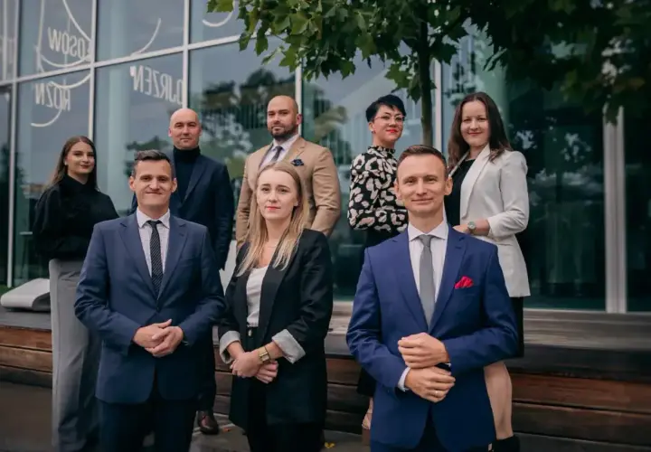 Grupa prawników w eleganckich strojach pozuje przed nowoczesnym budynkiem.
