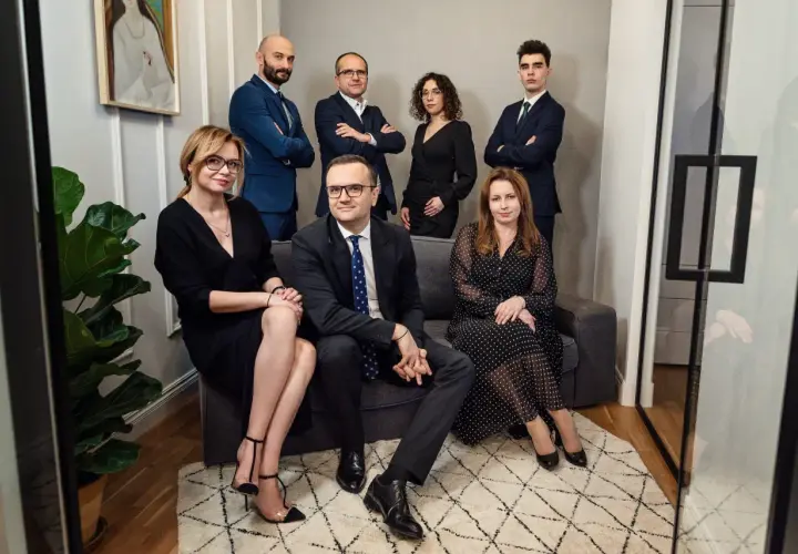 Grupa prawników w eleganckich strojach pozuje do zdjęcia w nowoczesnym wnętrzu.