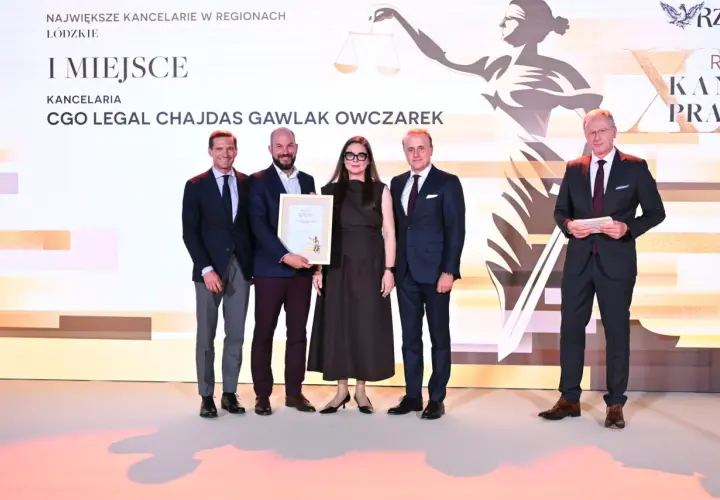 Pięć osób w eleganckich strojach pozuje do zdjęcia na tle sceny z grafiką i napisem "I MIEJSCE".
