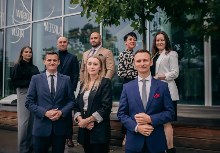 Grupa prawników w eleganckich strojach pozuje przed nowoczesnym budynkiem.