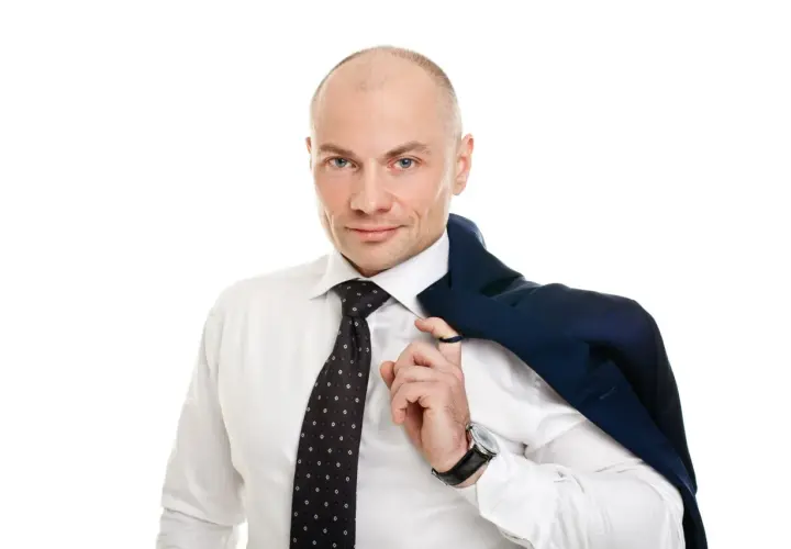 Łysy mężczyzna w białej koszuli i krawacie, z marynarką na ramieniu.