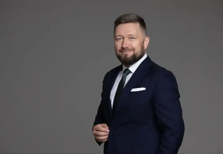 Portret mężczyzny w granatowym garniturze, białej koszuli i zielonym krawacie, z brodą i niebieskimi oczami.