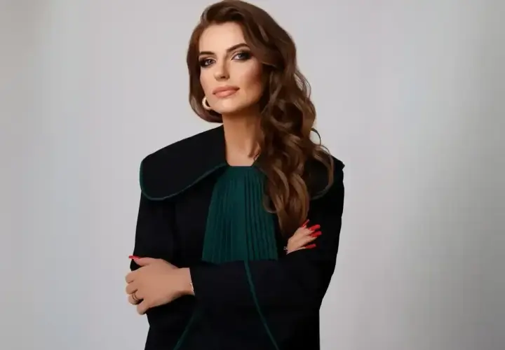 Kobieta w todze prawniczej, z rękami skrzyżowanymi na piersi, na jasnym tle.