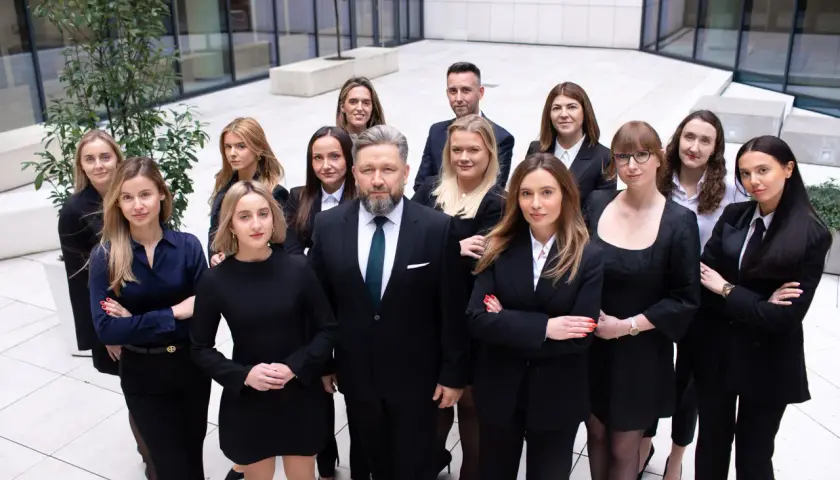 Grupa prawników w garniturach i sukienkach stoi przed nowoczesnym budynkiem.