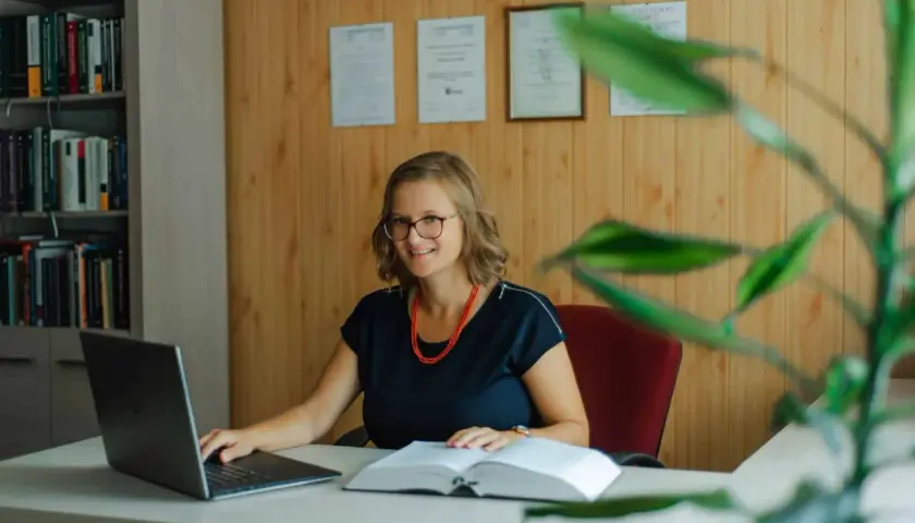 Uśmiechnięta prawniczka przy biurku z laptopem i książką. Dowiedz się, ile kosztuje sprawa o zasiedzenie u adwokata.