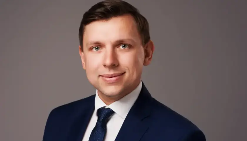 Portret mężczyzny w granatowym garniturze i krawacie na szarym tle.