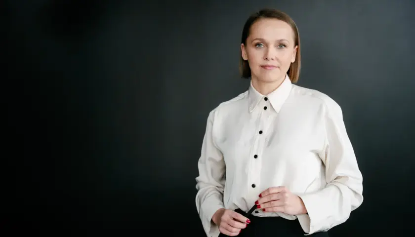 Kobieta w białej koszuli i czarnych spodniach na ciemnym tle.