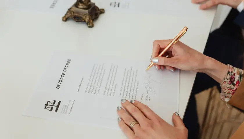 Dłoń podpisuje dokument "DIVORCE DECREE". Dowiedz się, jak napisać pozew o rozwód bez orzekania o winie.