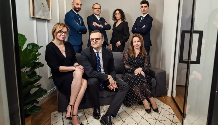 Grupa prawników w eleganckich strojach pozuje do zdjęcia w nowoczesnym wnętrzu.