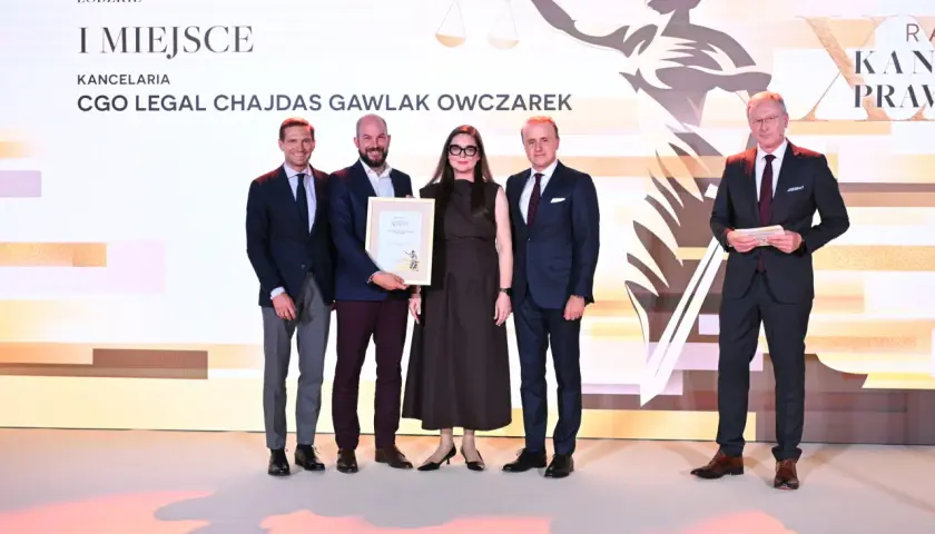 Pięć osób w eleganckich strojach pozuje do zdjęcia na tle sceny z grafiką i napisem "I MIEJSCE".