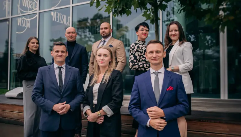 Grupa prawników w eleganckich strojach pozuje przed nowoczesnym budynkiem.