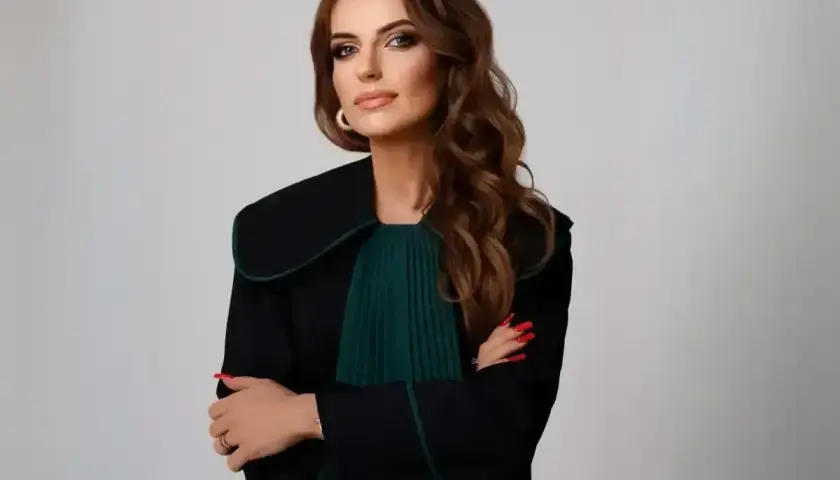 Kobieta w todze prawniczej, z rękami skrzyżowanymi na piersi, na jasnym tle.