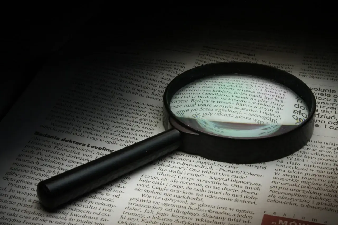 Lupa powiększa tekst, symbolizując dociekliwość i spostrzegawczość – kluczowe cechy dobrego detektywa.