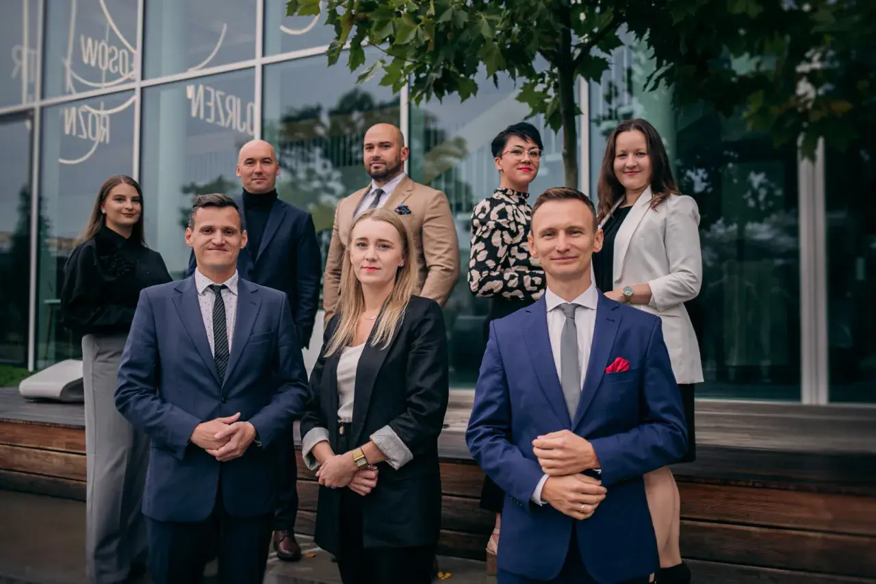 Grupa prawników w eleganckich strojach pozuje przed nowoczesnym budynkiem.