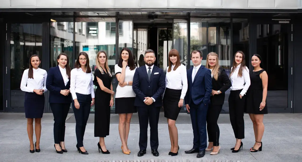 Grupa prawników w eleganckich strojach stoi przed nowoczesnym budynkiem.