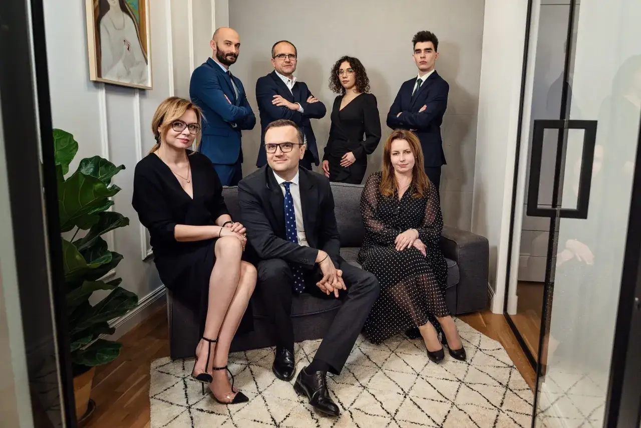 Grupa prawników w eleganckich strojach pozuje w nowoczesnym wnętrzu.