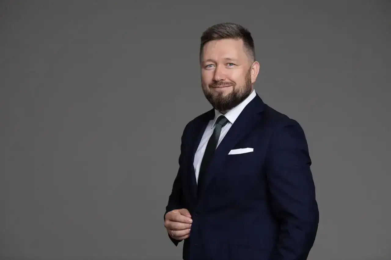 Portret mężczyzny w granatowym garniturze, białej koszuli i zielonym krawacie, z białą poszetką.