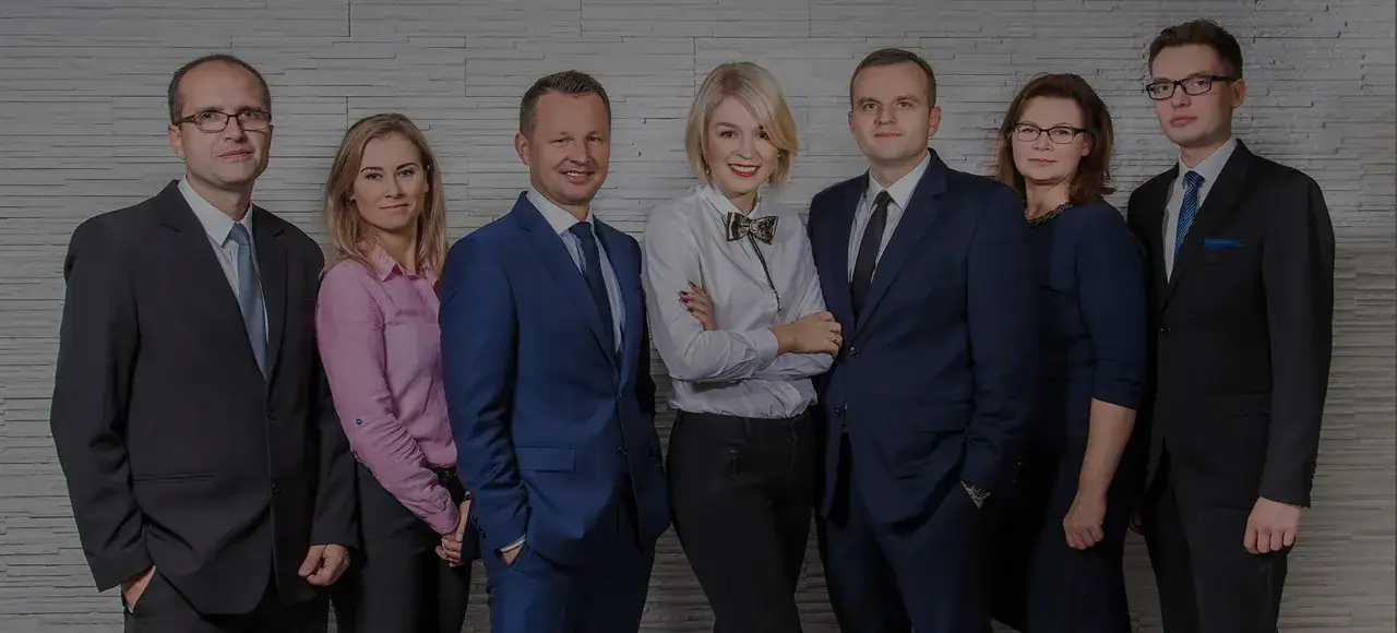 Zespół prawników w eleganckich strojach na tle kamiennej ściany.