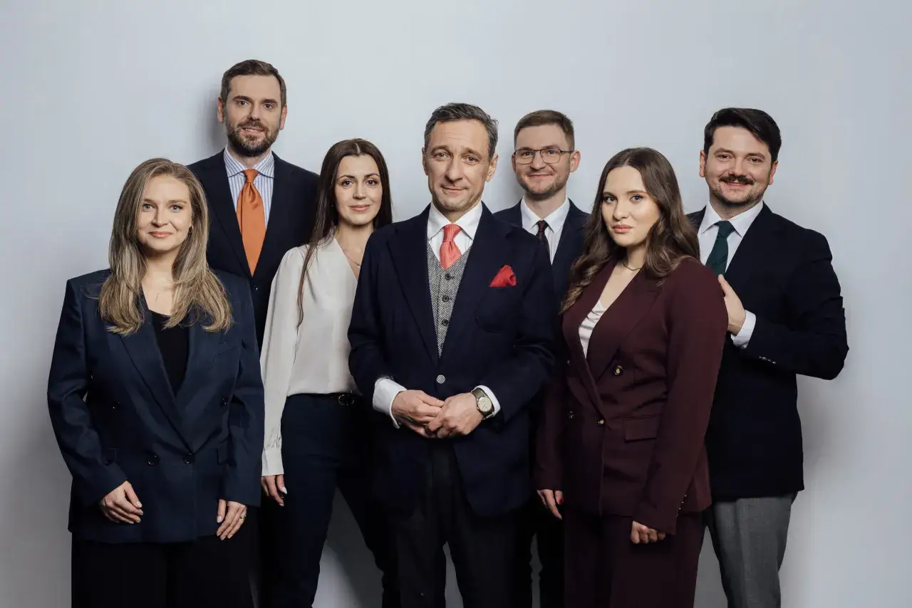 Grupa prawników w eleganckich garniturach i kostiumach pozuje do zdjęcia na jasnym tle.